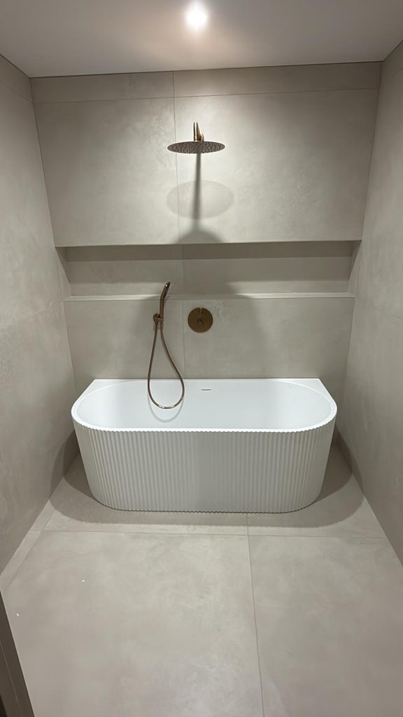 Salle de bains avec baignoire blanche, carrelage beige et robinetterie en cuivre brossé.